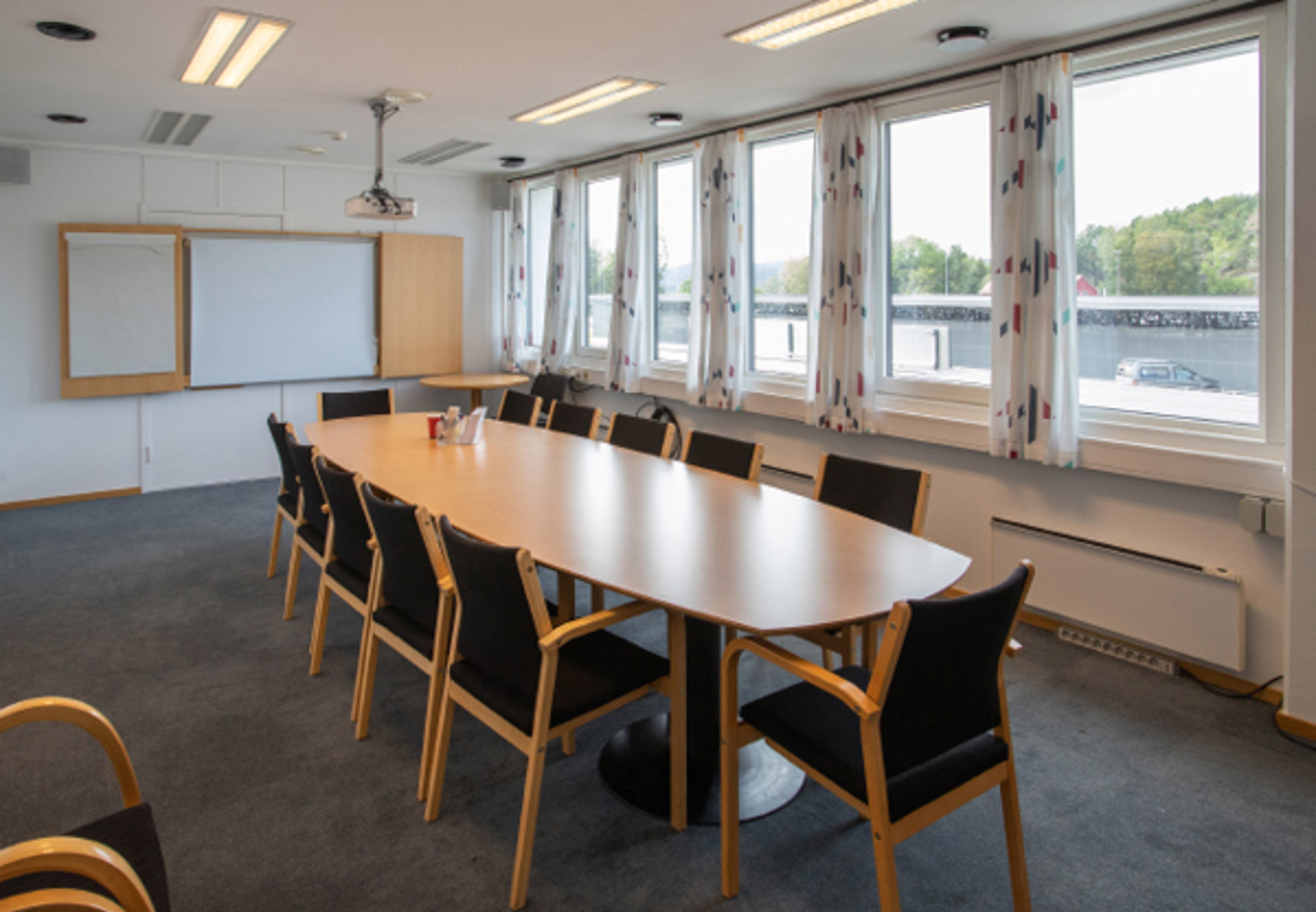 Møterom med ovalt bord i lyst tre og stoler i lyst tre og sort stoff