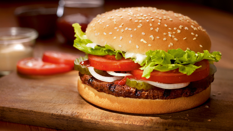Delicious burger with beef patty, fresh lettuce, tomato slices, onions, pickles, and sesame seed bun on wooden board