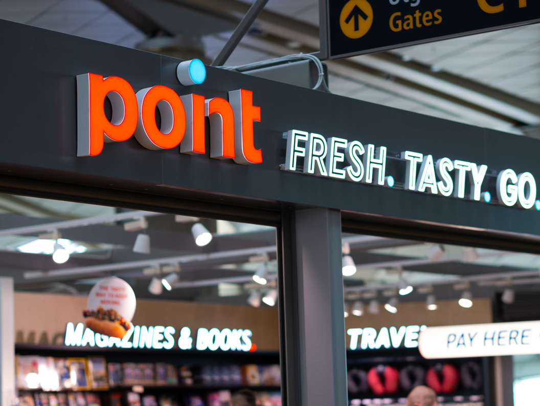 Butikkskilt med teksten "point" og slagordet "FRESH. TASTY. GO." i ein flyplassbutikk