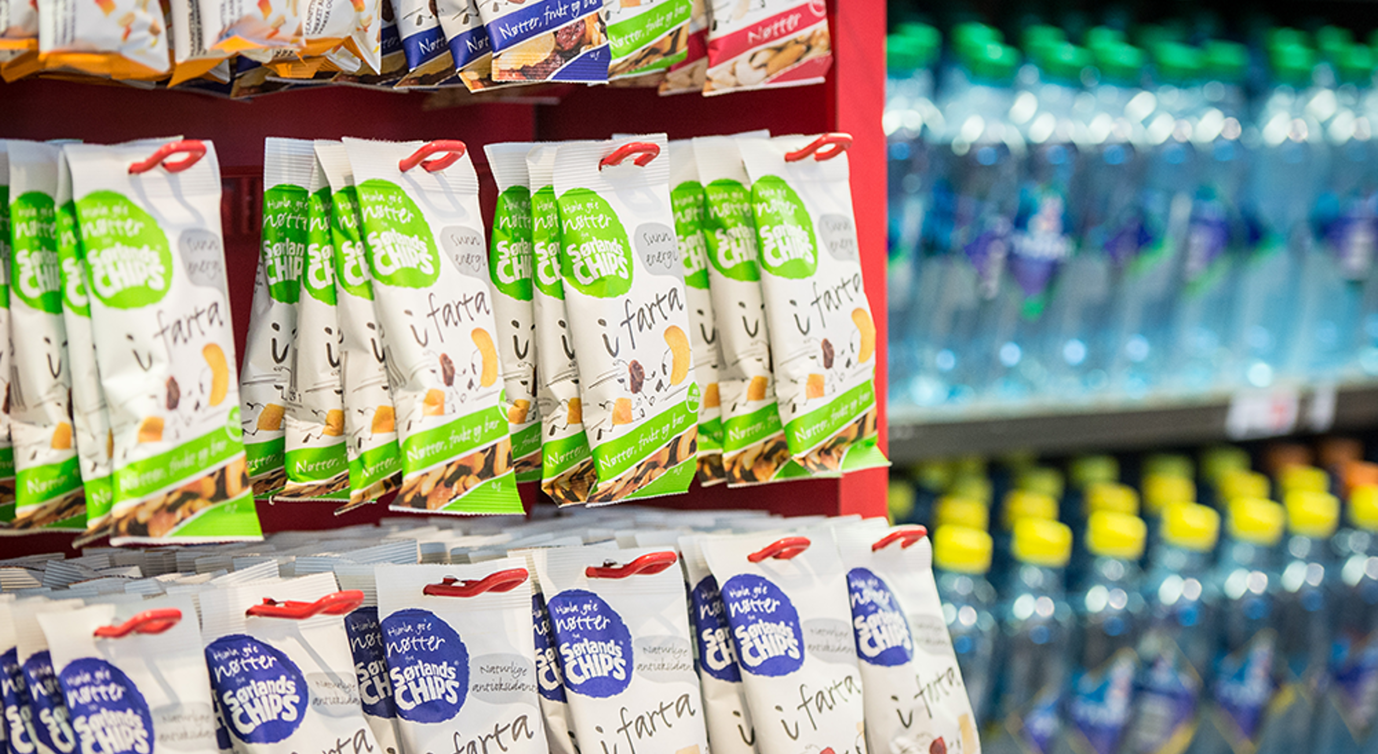 Snacksdisplay i en dagligvarebutikk med hyller som viser ulike pakker med chips og flaskevann i bakgrunnen