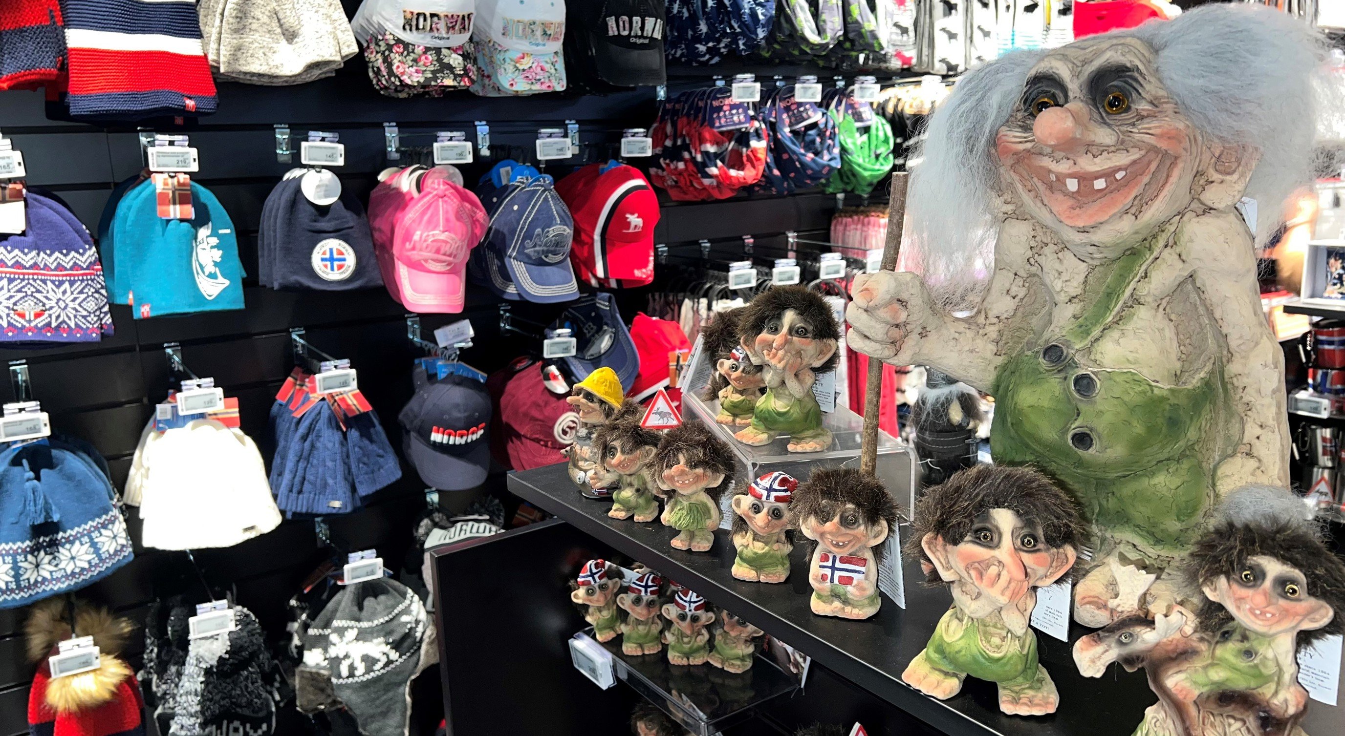 Troll figurines and assorted hats on display in a Norwegian souvenir shop, featuring traditional designs and vibrant colors