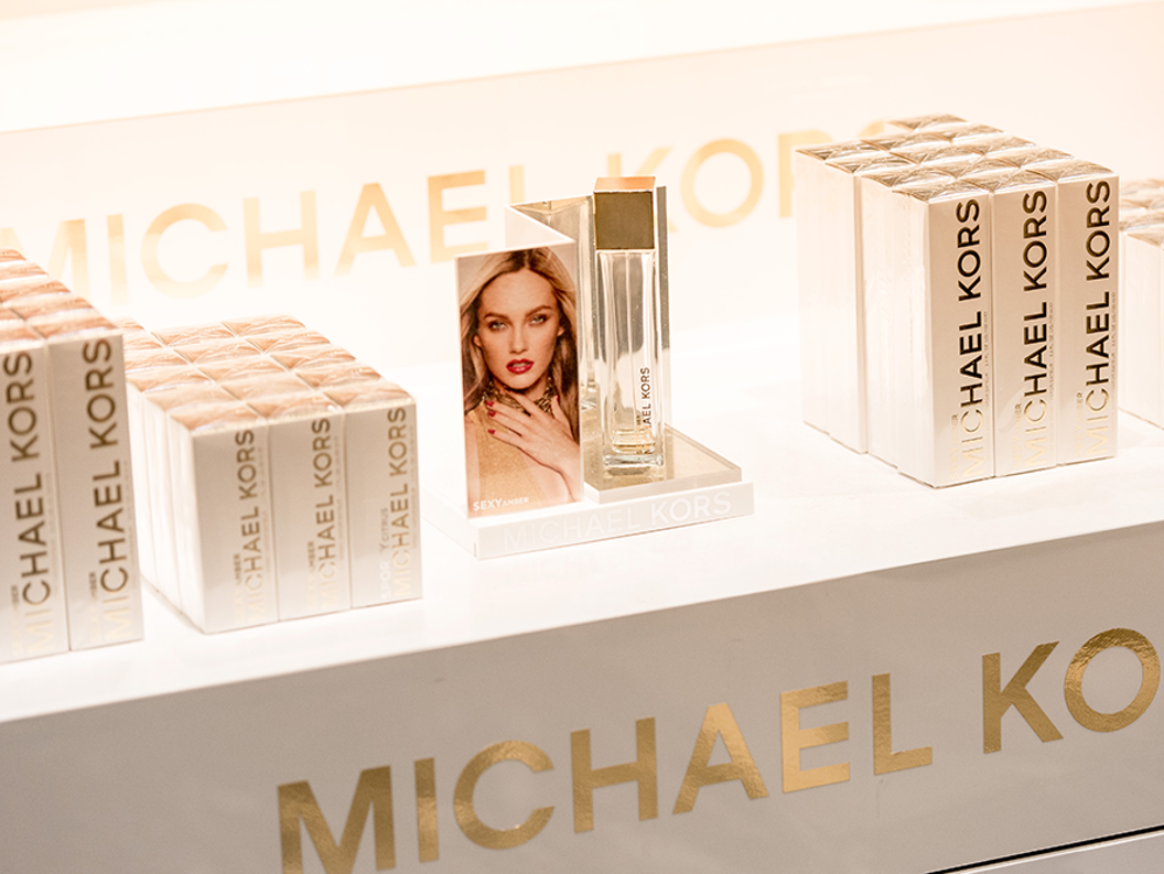 Display of Michael Kors "Sexy Amber" perfume with branded packaging boxes arranged neatly on a store shelf