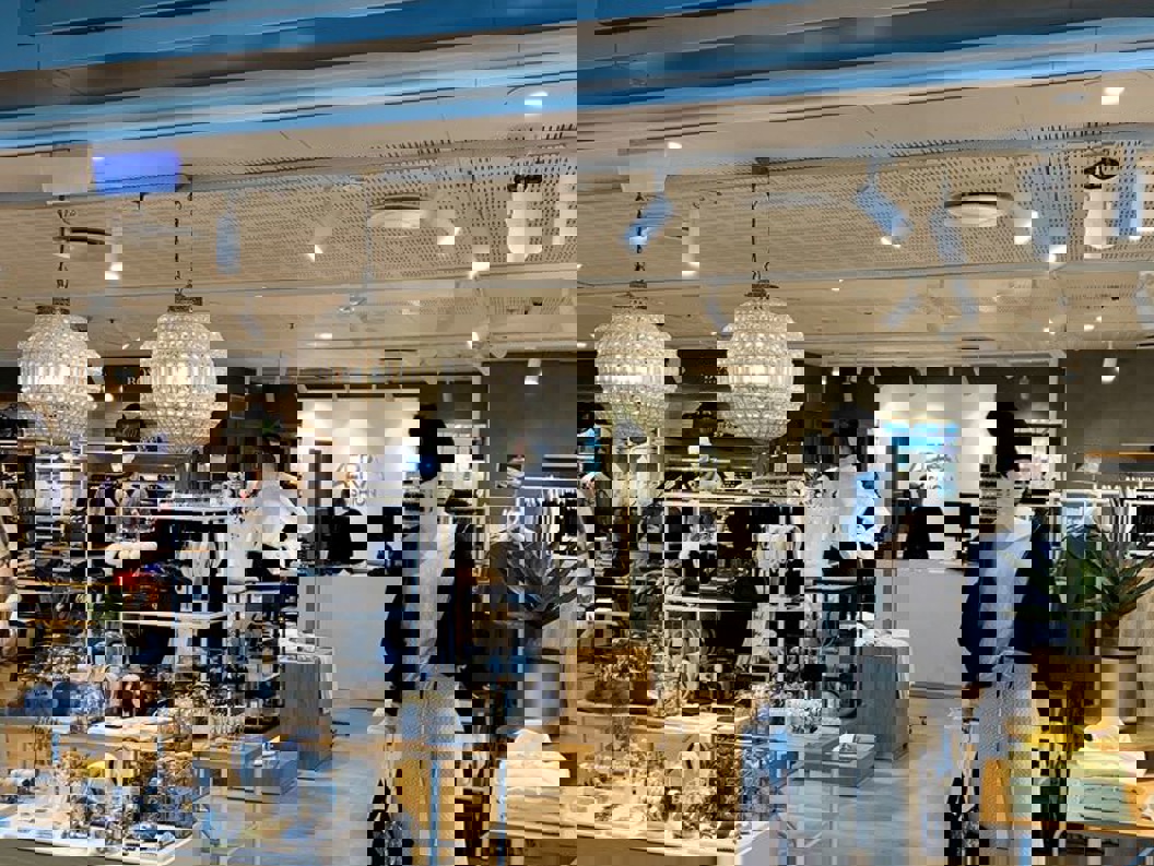 Fashion retail store entrance showcasing stylish mannequins and accessories, with prominent "AERA Fashion" signage above. The interior displays a variety of clothing and jewelry under warm lighting