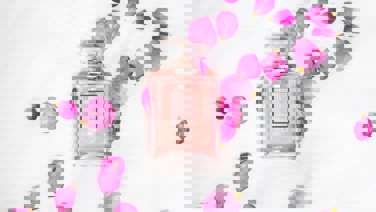 Rosa parfymeflaske omgitt av rosa roseblader på en hvit bakgrunn, som skaper en elegant og feminin estetikk