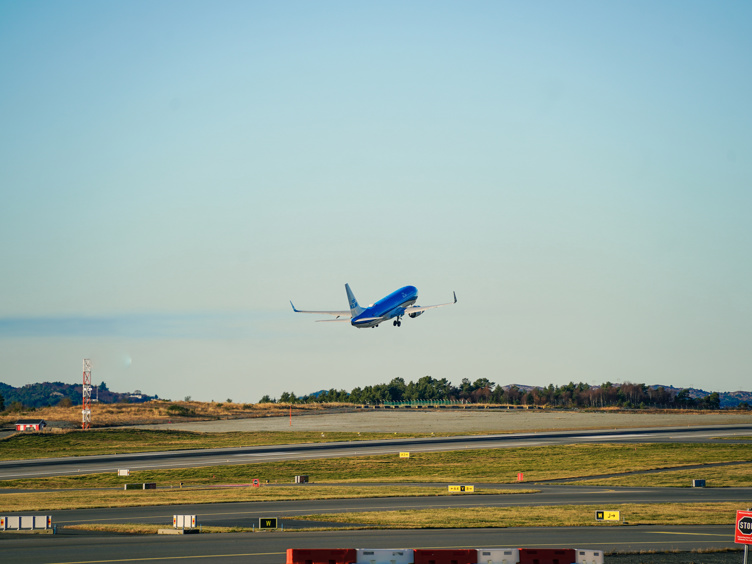 A blue passenger plane takes off from the runway at the airport with a clear sky in the background.