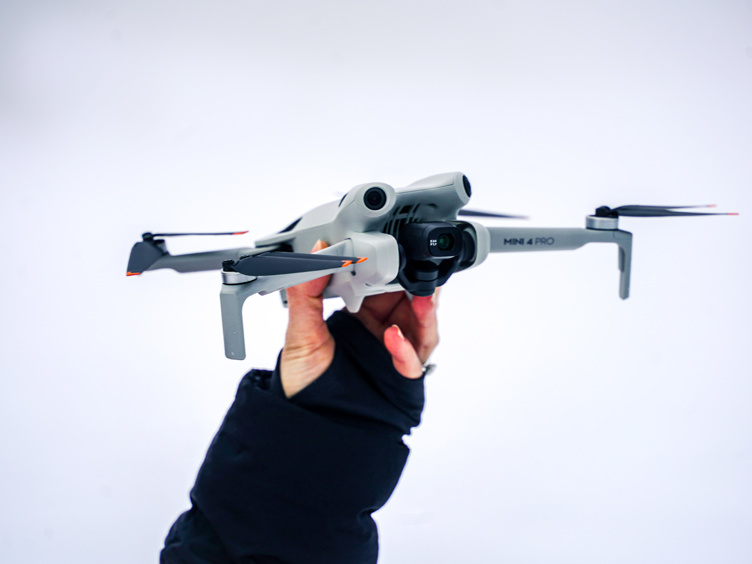 Hand holding a gray Mini 4 Pro drone against a white background, ready for takeoff.