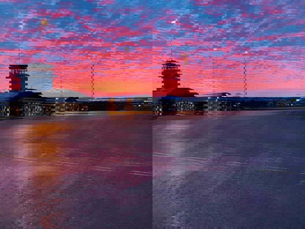 Lakselv flyplass ved solnedgang med fargerik himmel i rosa og blåtoner, terminalbygning og kontrolltårn.