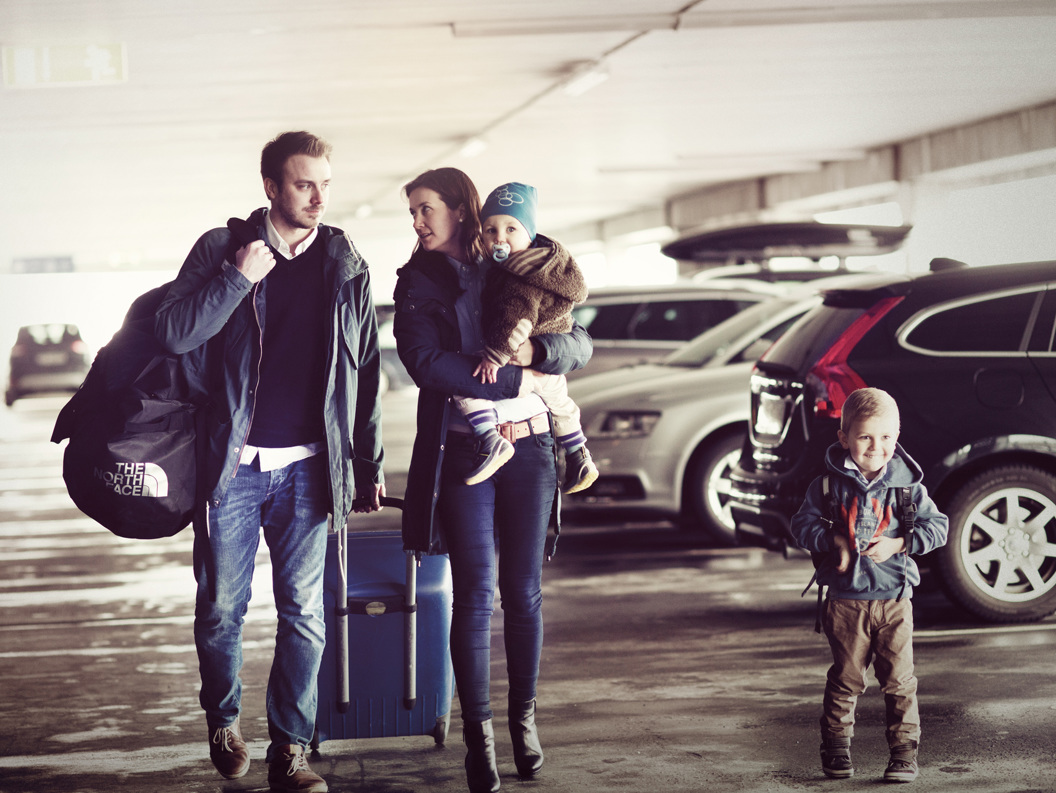 Family of four with luggage in a parking garage, ready for travel. Parents and children stand among cars with suitcases and backpacks.