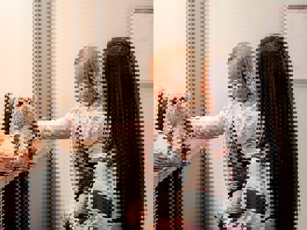 En dame med langt brunt hår står med en liten jente på armen foran en skranke hvor jenta får tilbake en bamse hun har glemt på flyet eller lignende.