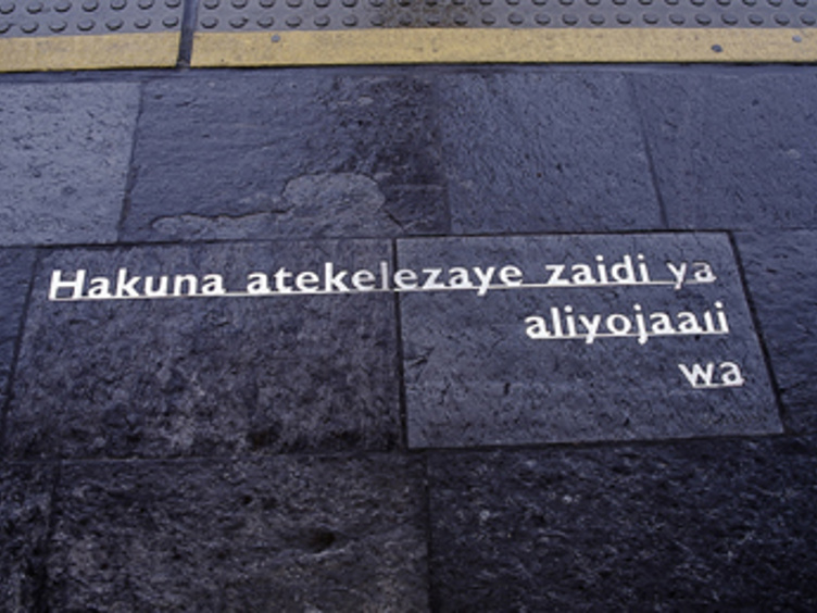 Inngravert tekst på mørke steinfliser ved et fortau, med gul linje øverst