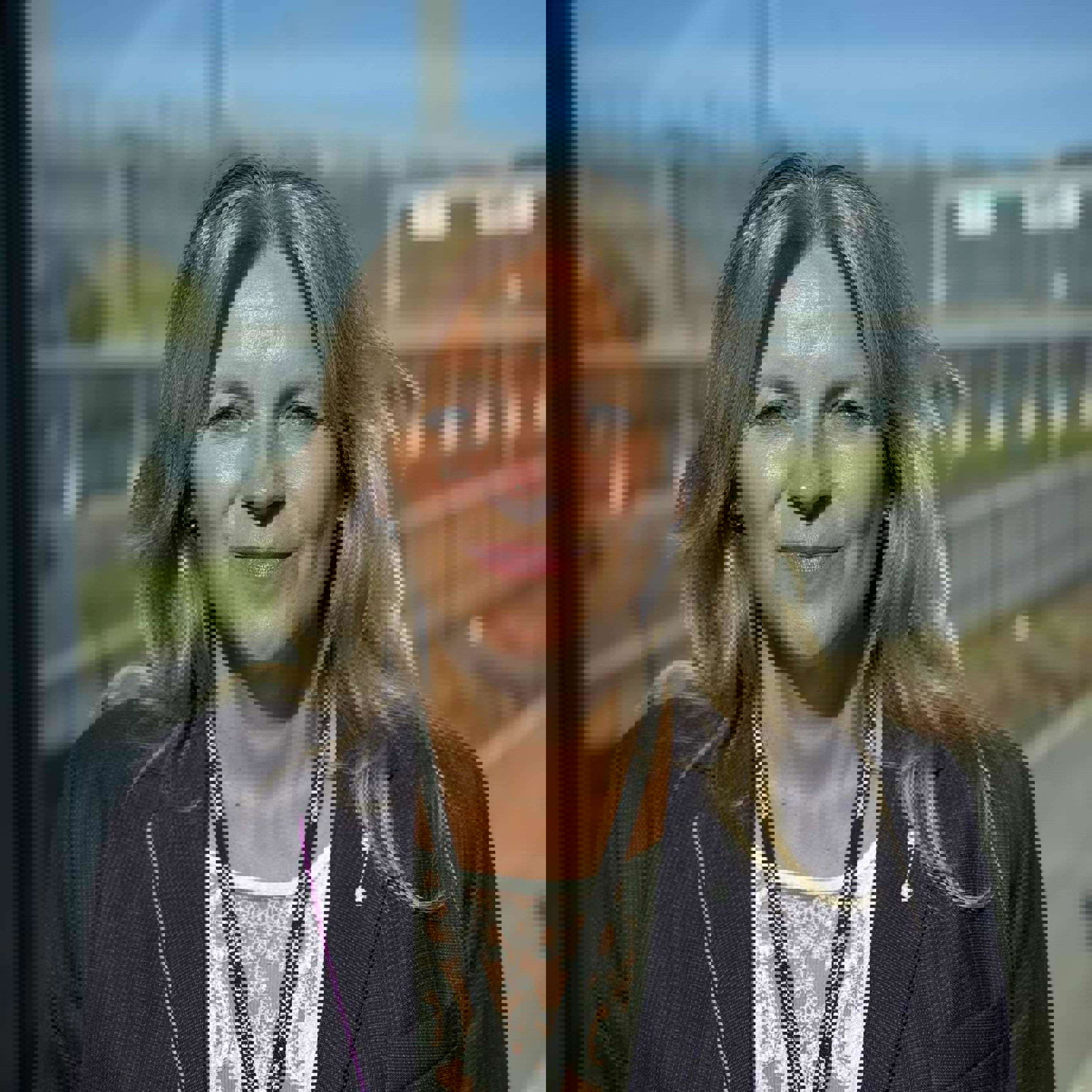 Woman in formal attire smiling outdoors with clear weather and buildings in the background.