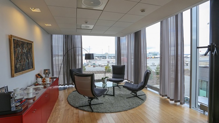 Bright meeting room with a view of the airport, elegantly decorated with modern chairs, a round table, and art on the wall.