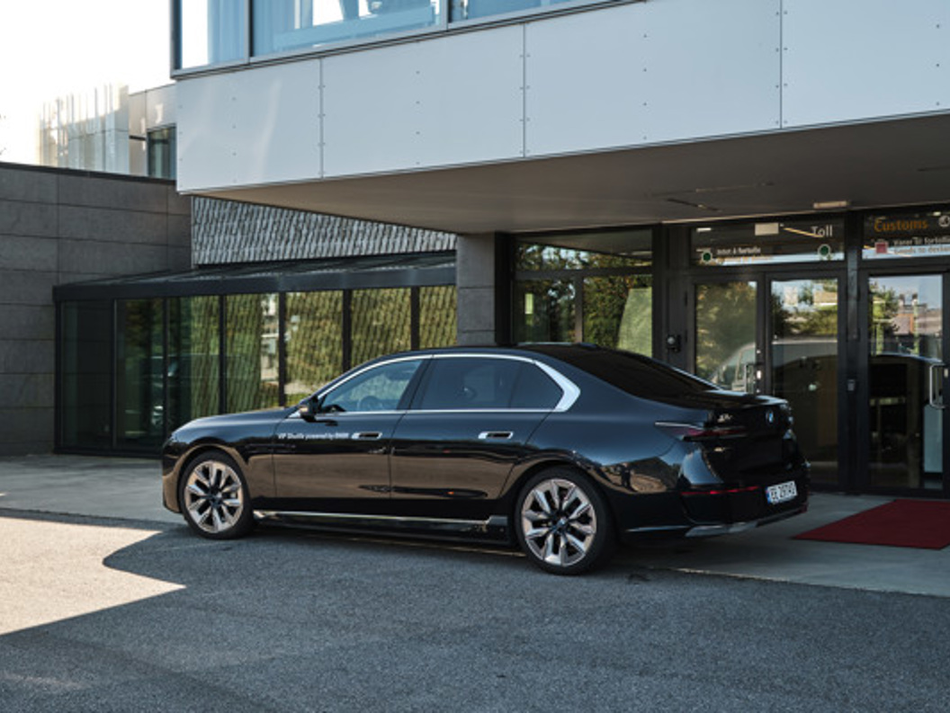 Black luxury sedan parked in front of a modern building in sunlight.