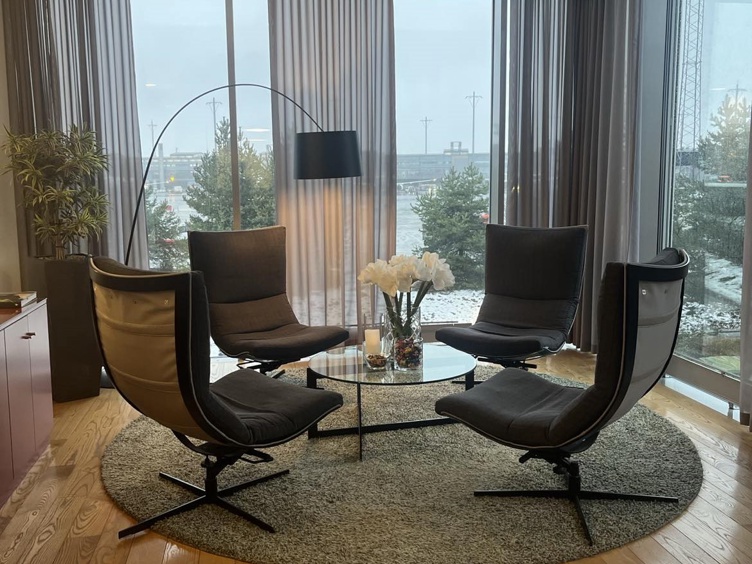 Modern living room with four black chairs around a glass table, decorated with white flowers, in a room with large windows and a view of a winter landscape.