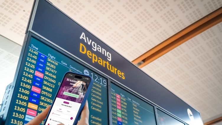 A traveler holds a mobile phone in front of a departures board at Oslo Airport. The phone screen shows a webpage for purchasing an eSIM for travel. In the background, multiple flight departures on a digital board.