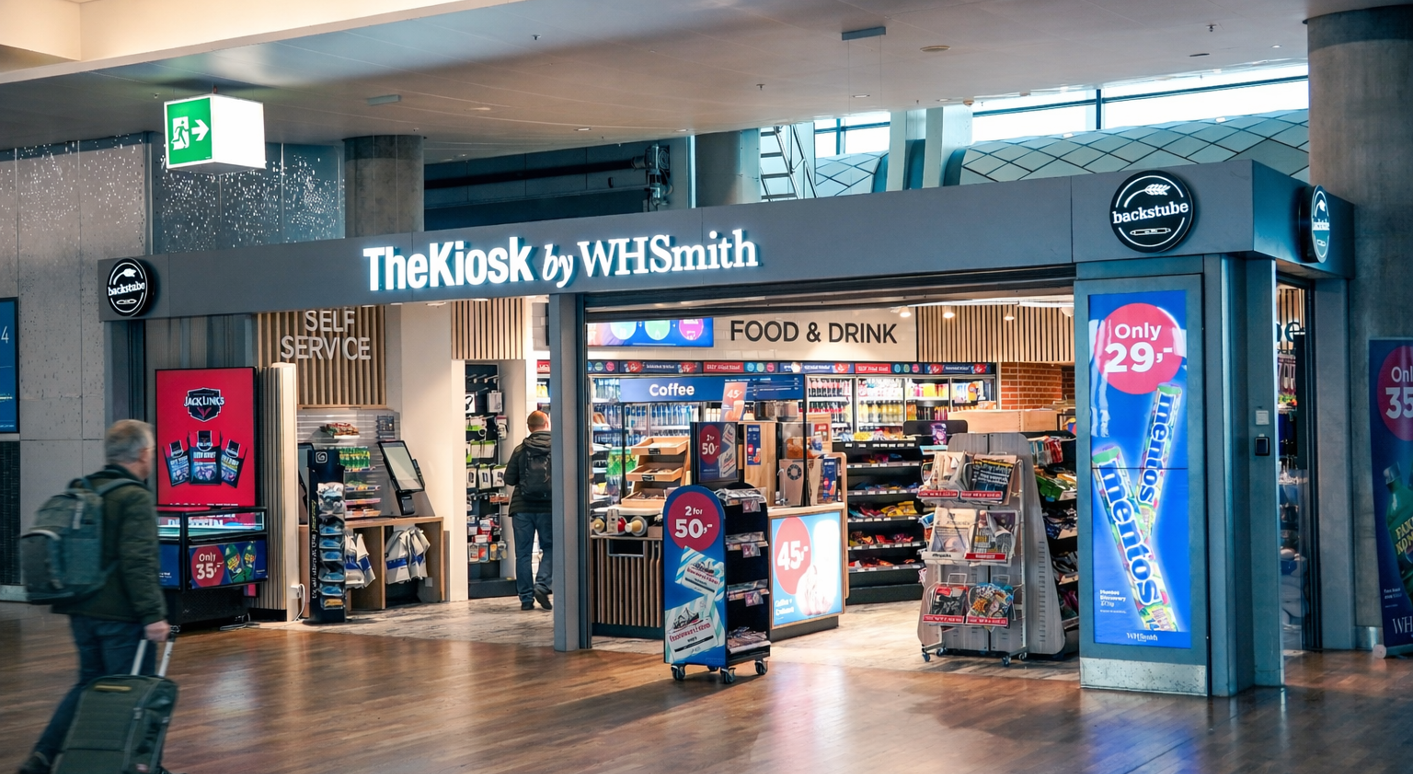 Moderne WHSmith-kiosk på en flyplass som tilbyr nødvendighetsartikler, snacks og drikkevarer under levende belysning