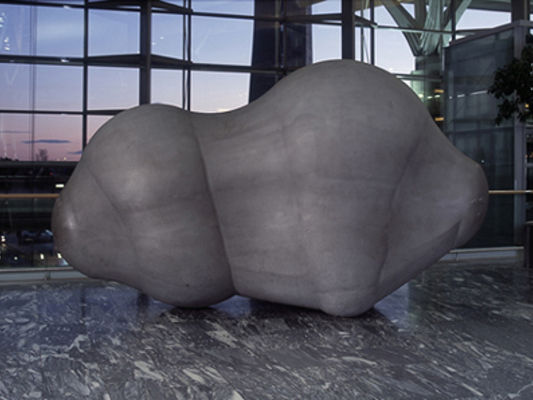 Skulptur av en abstrakt, organisk formet stein, plassert i en moderne bygning med store vinduer og marmorgulv
