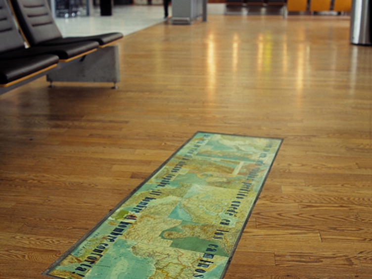 Kartmotiv gulvteppe i flyplasslounge med treparkett og ledige seter i bakgrunnen