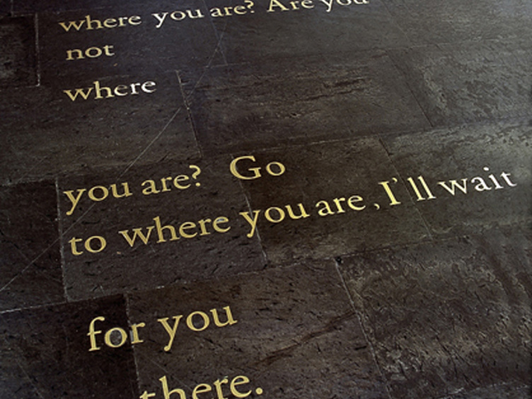 Tekst inngravert i gulvfliser, som stiller spørsmål om personlig tilstedeværelse og lover å vente der man befinner seg
