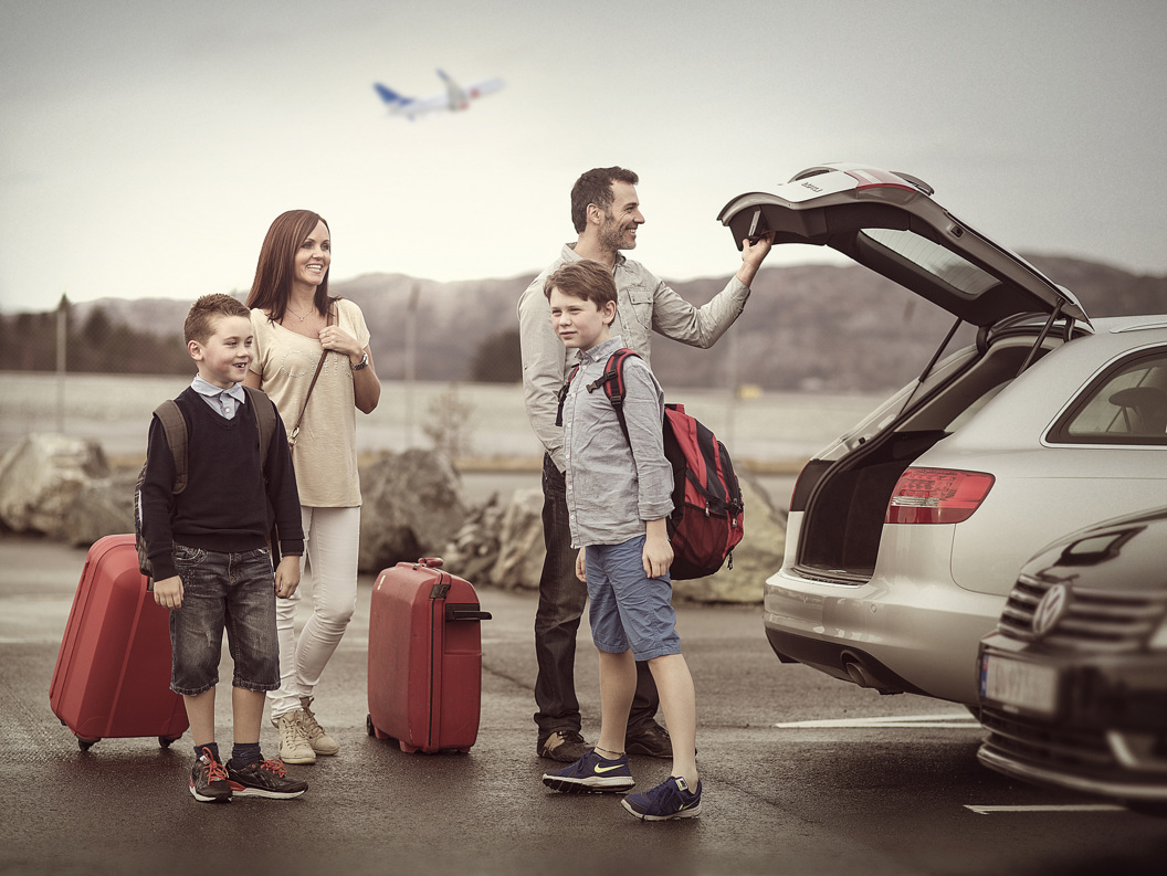 Family at parking lot with luggage and car, ready for travel. Plane in the background.
